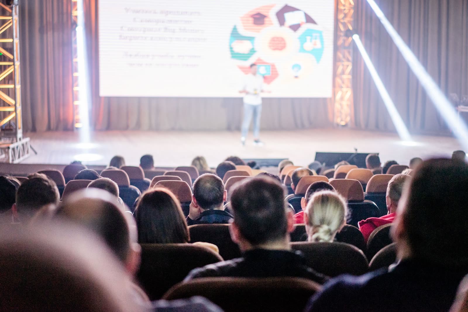 An audience watches a presentation under stage lights.
